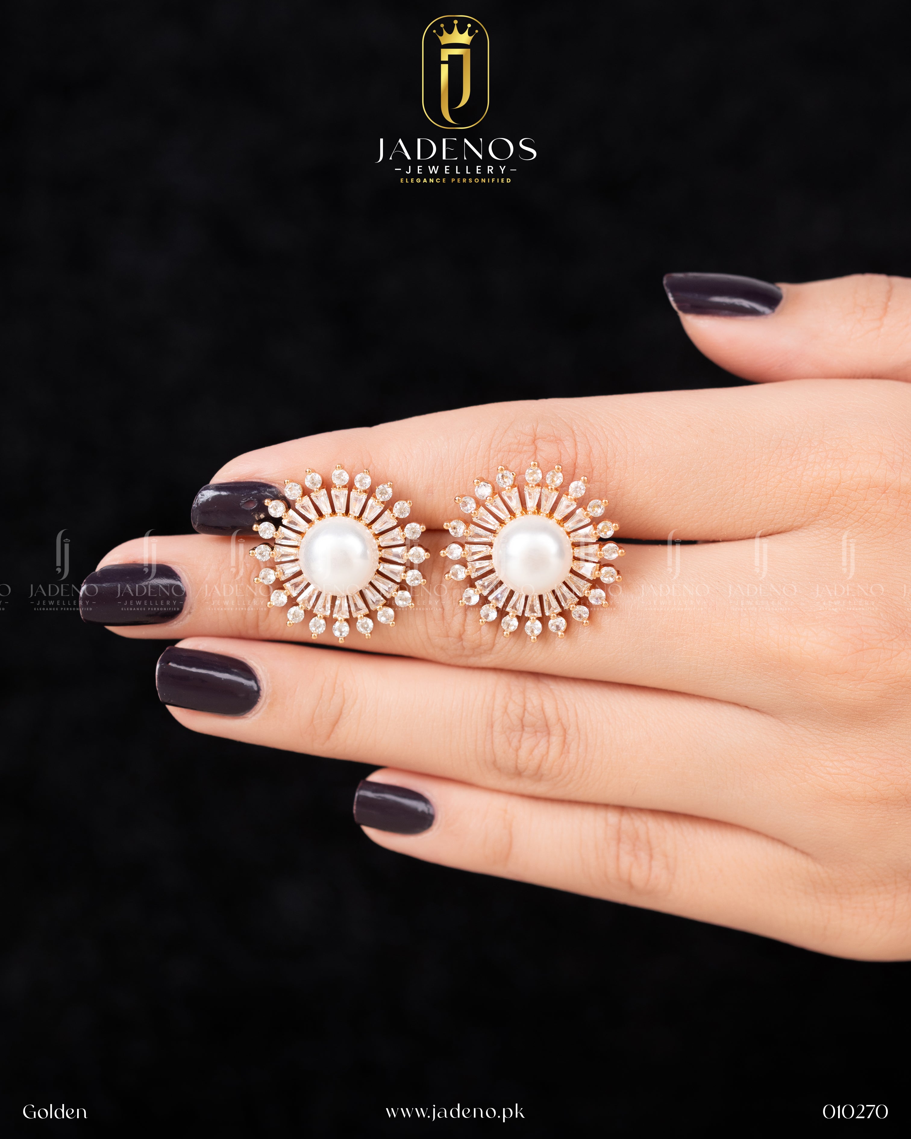 A pair of golden Bloomy Studs featuring a central pearl surrounded by sparkling crystal stones in a sunburst design, held by a hand with dark nails.